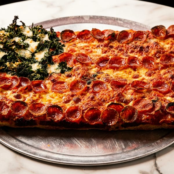 Rectangular pizza resembling an American flag with pepperoni stripes and kale with cheese stars.