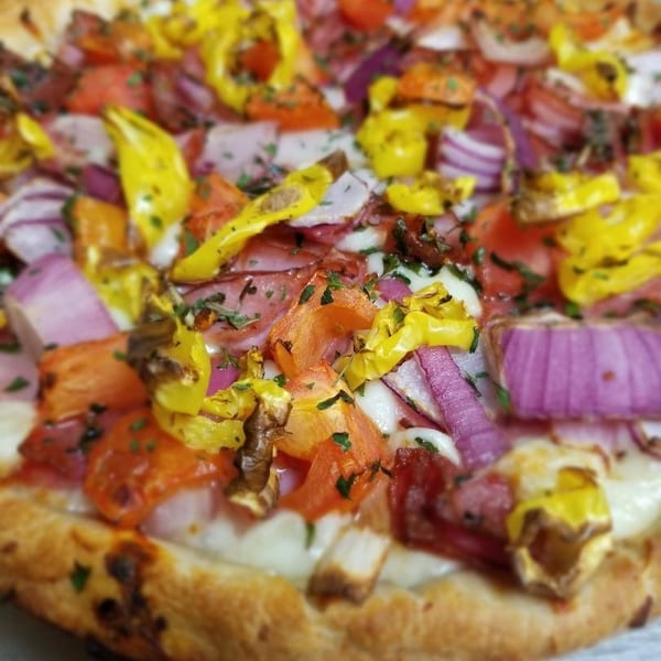 Close-up of a pizza with red onions, yellow peppers, tomatoes, and herbs.