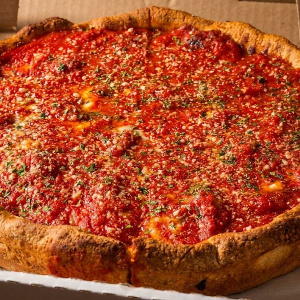 Whole deep-dish pizza with vibrant red sauce, grated cheese, and herbs in a cardboard box.